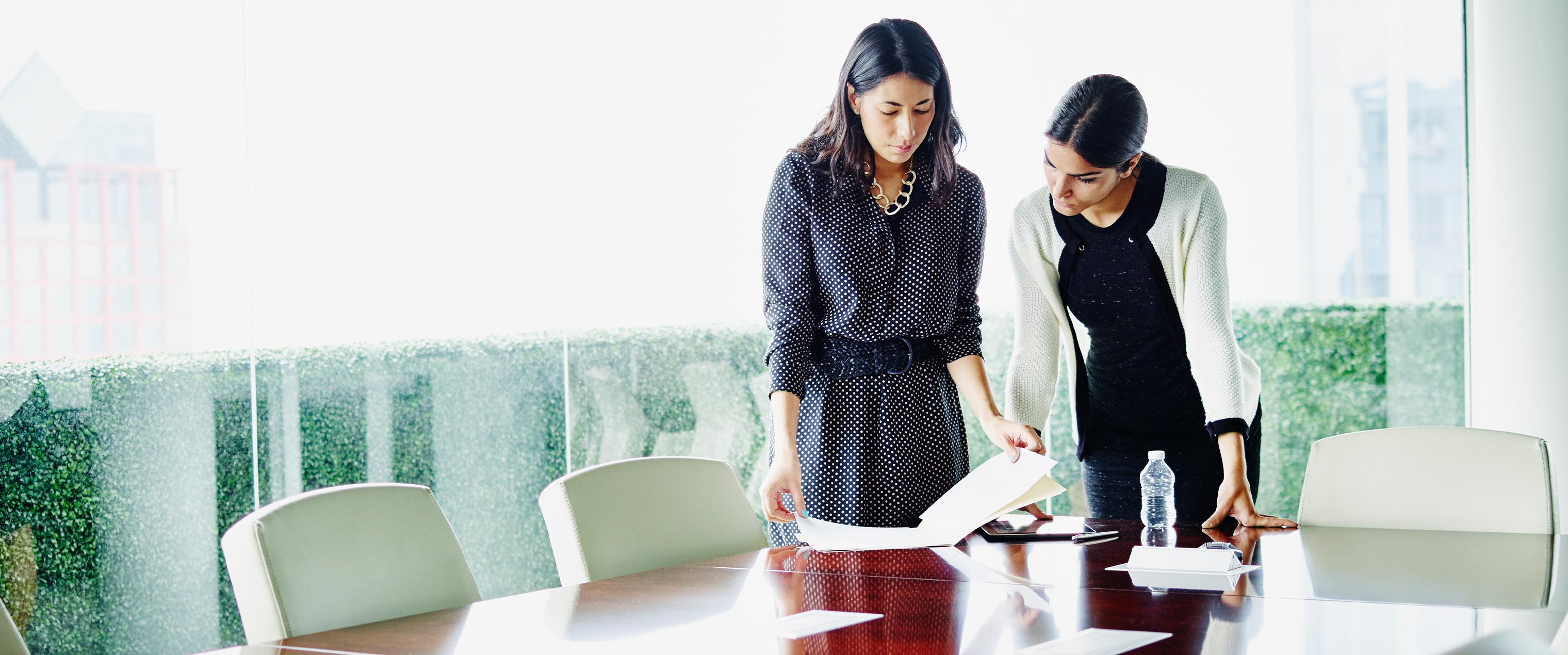 Two women standing next to a table looking at a folder