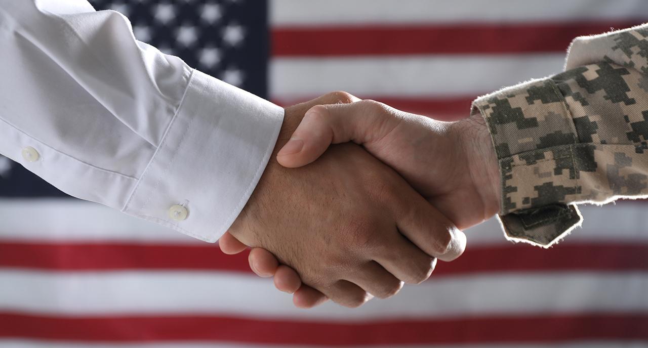 Servicemen shaking hands in front of the American flag