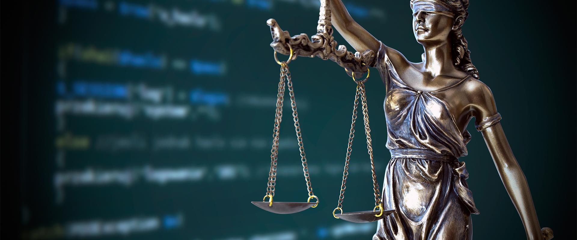 Statue of judge with scales in front of computer screen of code