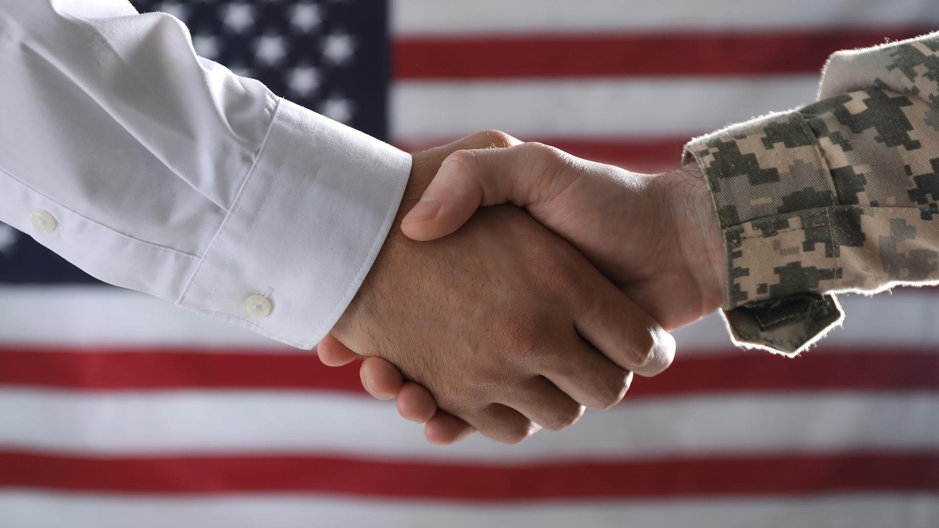 Servicemen shacking hands in front of American flag