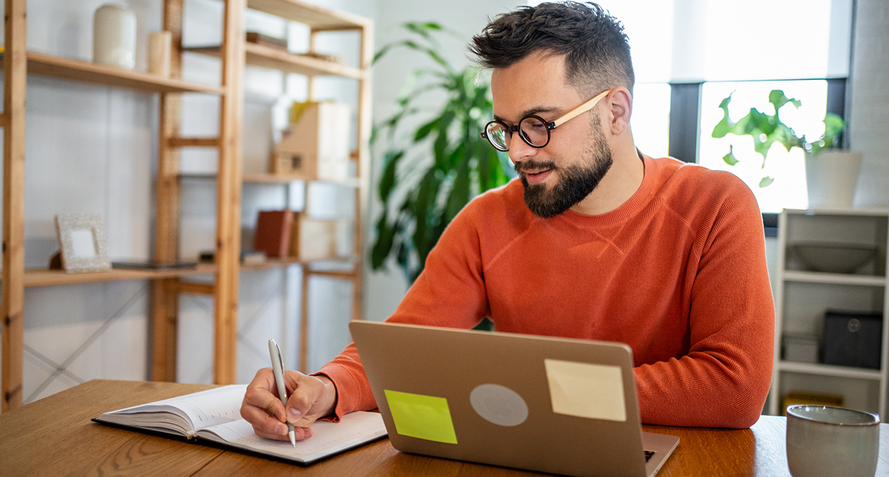 Man in his 30s working at his desk, wearing an orange sweater 