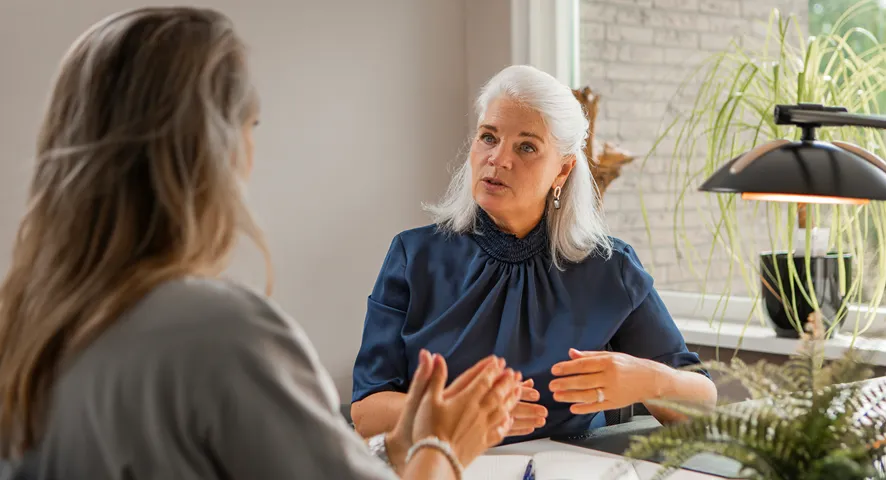 Two middle aged women speaking together in the office