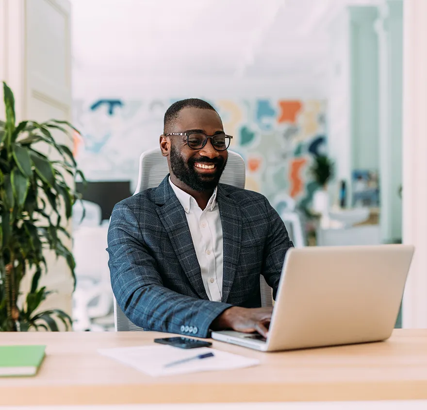 Man in a suit smiling while working on his laptop