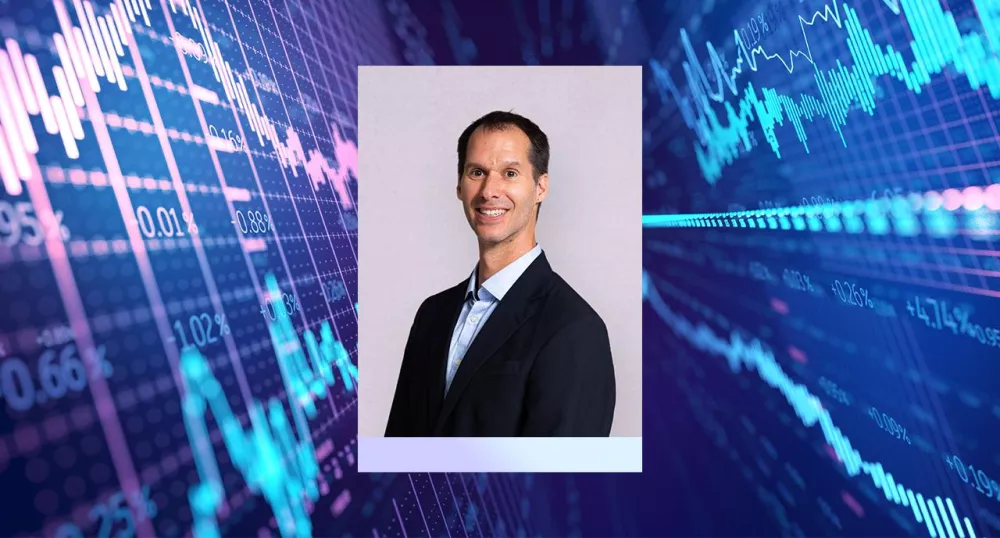 Photo of Eric Ludwig with stock market graphs behind him