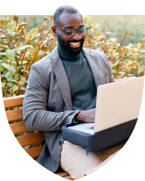 Man typing on his laptop and smiling in the park