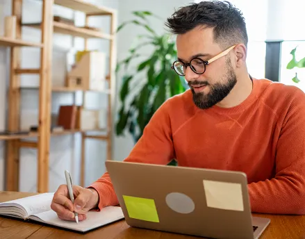 Man in his 30s working at his desk, wearing an orange sweater 